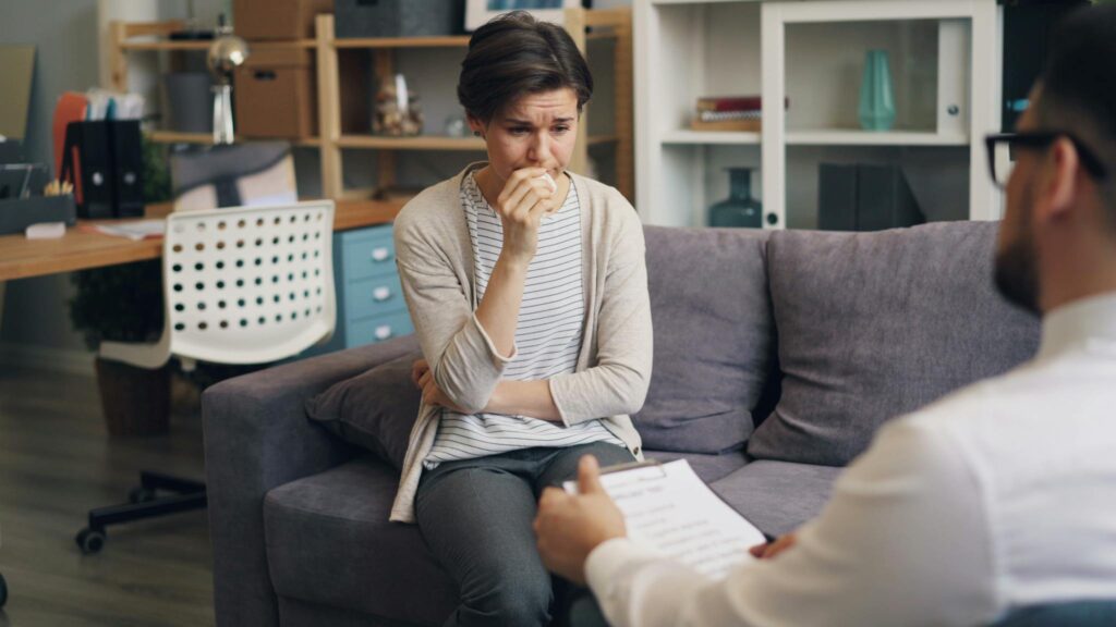 A young woman expresses emotions during a therapy session, consulting with a psychologist indoors.